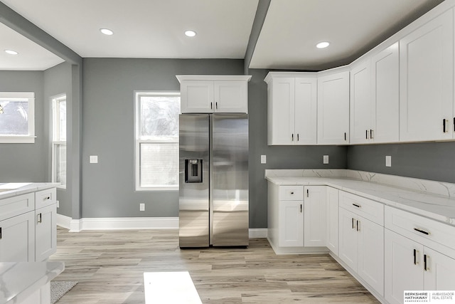 kitchen featuring white cabinets, baseboards, light stone counters, and stainless steel refrigerator with ice dispenser