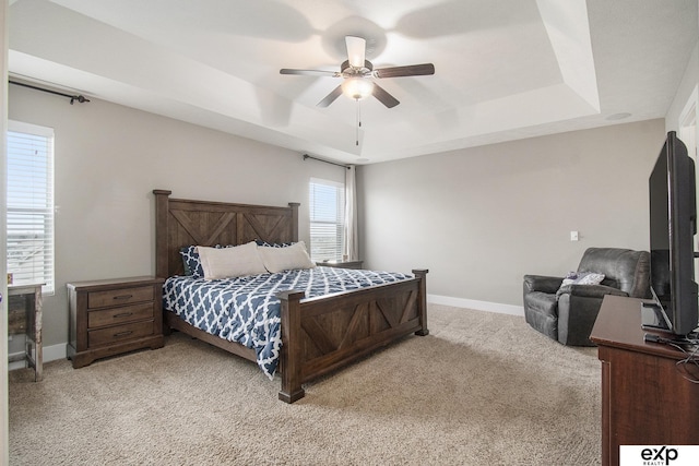 carpeted bedroom with ceiling fan, a tray ceiling, and baseboards