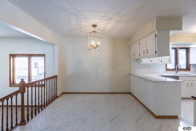 kitchen with white cabinets, decorative light fixtures, marble finish floor, light countertops, and a sink