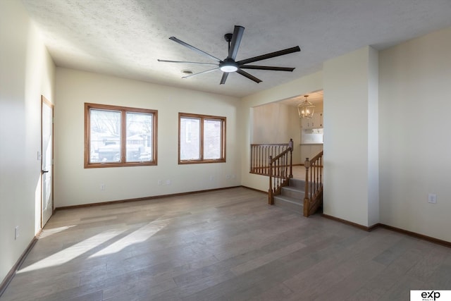 empty room with ceiling fan with notable chandelier, a textured ceiling, baseboards, and wood finished floors