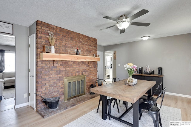 dining room featuring a textured ceiling, a fireplace, baseboards, and light wood-style floors