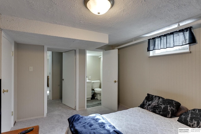 bedroom with ensuite bath, a textured ceiling, and light colored carpet