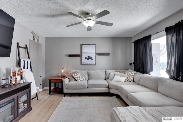 living room with light wood finished floors, a textured ceiling, baseboards, and a ceiling fan