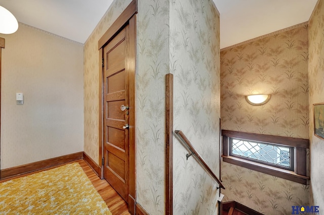 stairway featuring wallpapered walls, baseboards, and wood finished floors