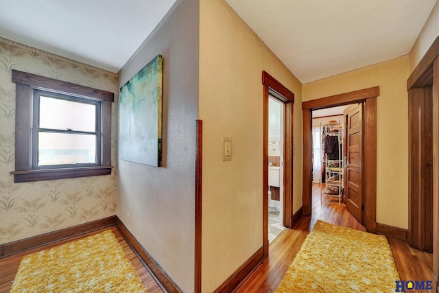 hall featuring wood finished floors, baseboards, and wallpapered walls