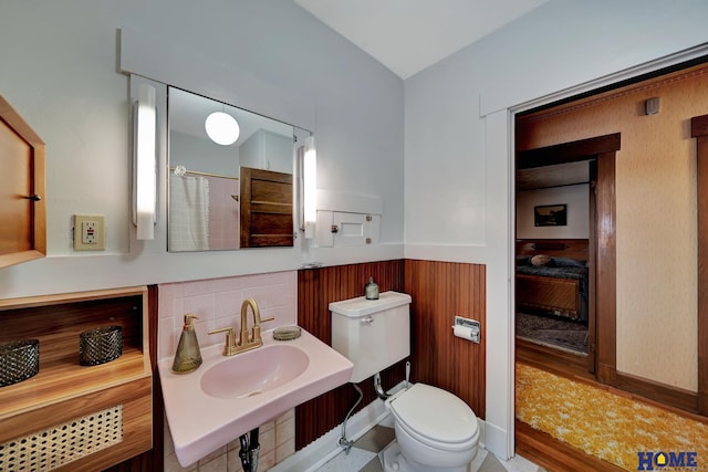 bathroom featuring toilet, a wainscoted wall, a shower with shower curtain, a sink, and ensuite bath