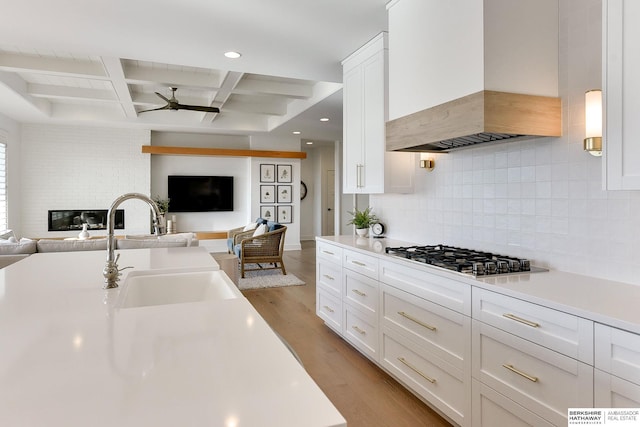 kitchen featuring premium range hood, a sink, white cabinetry, open floor plan, and light countertops