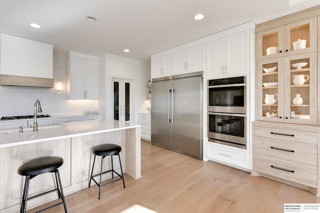 kitchen with light countertops, appliances with stainless steel finishes, glass insert cabinets, white cabinetry, and a kitchen breakfast bar