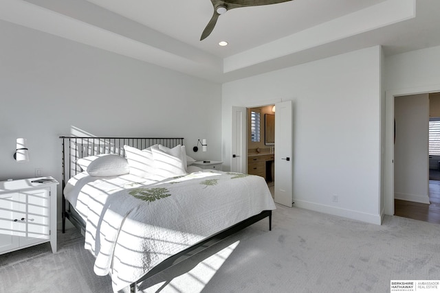 bedroom with a tray ceiling, recessed lighting, light carpet, connected bathroom, and baseboards