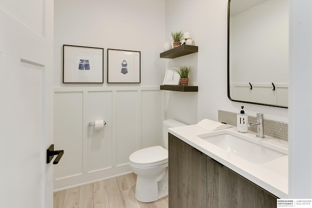 half bath with toilet, a decorative wall, wood finished floors, and vanity