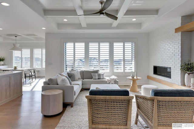 living area featuring a brick fireplace, light wood-style flooring, a ceiling fan, and a wealth of natural light