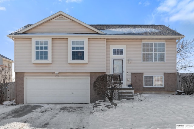 raised ranch with brick siding, fence, and an attached garage