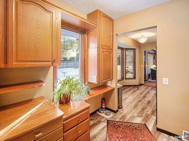 interior space with a textured ceiling, light countertops, light wood-style flooring, and baseboards