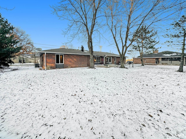 snow covered house with brick siding and central air condition unit