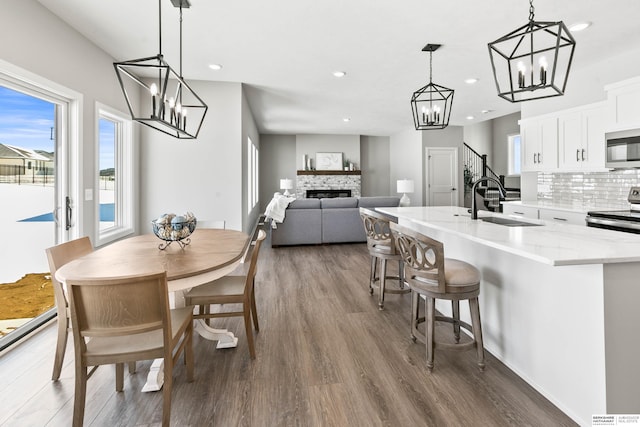 dining room featuring a chandelier, a stone fireplace, recessed lighting, wood finished floors, and stairway