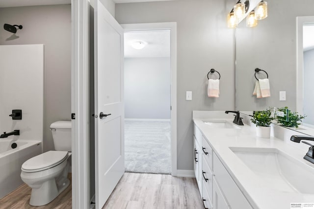 full bath with double vanity, a sink, toilet, and wood finished floors