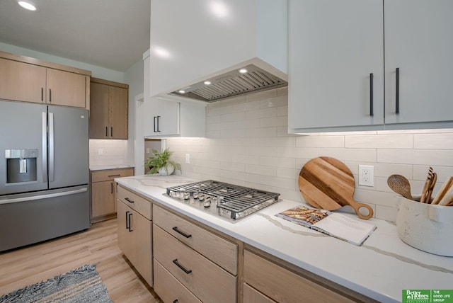 kitchen with light stone counters, light brown cabinets, appliances with stainless steel finishes, light wood finished floors, and custom range hood