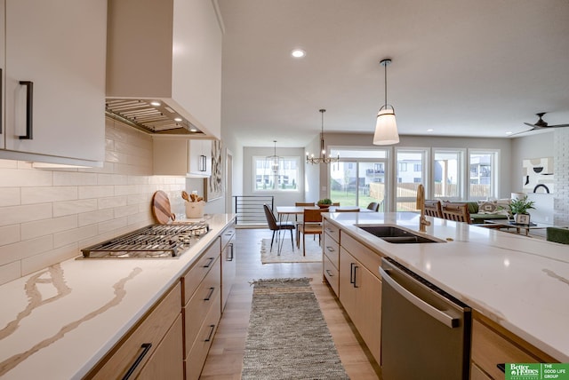 kitchen with pendant lighting, custom exhaust hood, stainless steel appliances, open floor plan, and a sink