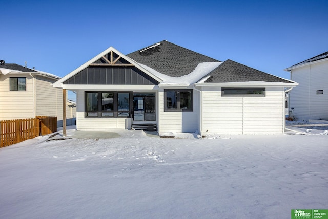 view of front facade featuring entry steps, a shingled roof, fence, and board and batten siding