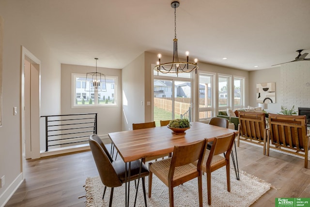 dining area with a healthy amount of sunlight, light wood-style flooring, a fireplace, and a notable chandelier