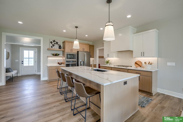 kitchen with pendant lighting, a center island with sink, stainless steel appliances, white cabinets, and a sink