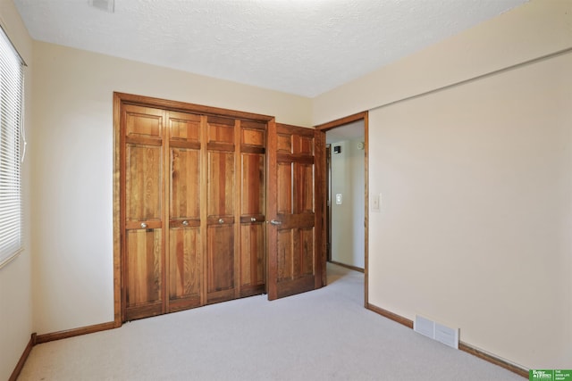 unfurnished bedroom with light carpet, a textured ceiling, a closet, and visible vents