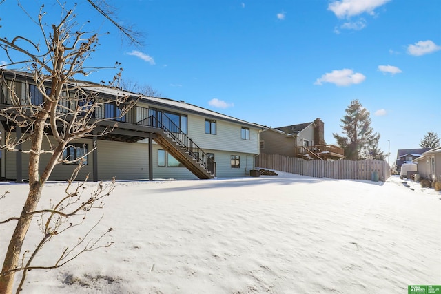 snow covered back of property featuring stairway and fence