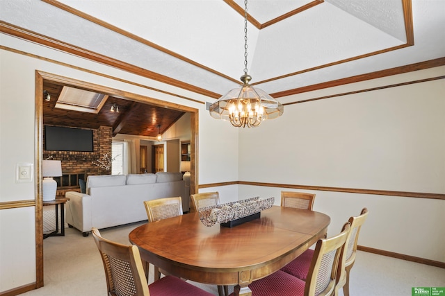 dining area featuring light carpet, baseboards, ornamental molding, a brick fireplace, and a notable chandelier