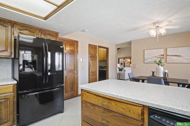 kitchen featuring brown cabinetry, light countertops, a textured ceiling, black appliances, and light tile patterned flooring