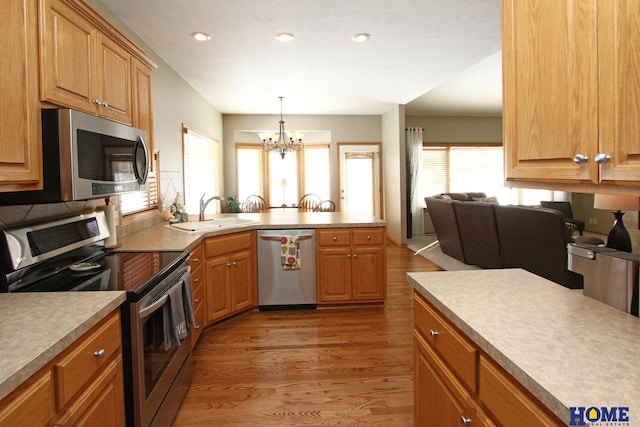 kitchen featuring a sink, light wood-style floors, light countertops, appliances with stainless steel finishes, and hanging light fixtures