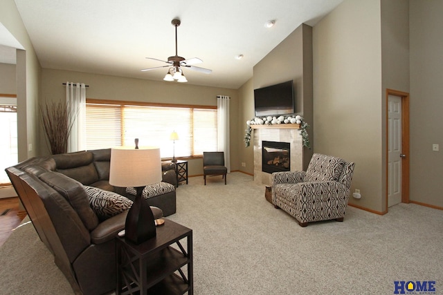 living room with ceiling fan, high vaulted ceiling, baseboards, a tiled fireplace, and carpet