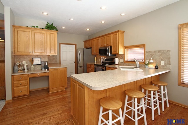 kitchen with light countertops, appliances with stainless steel finishes, built in study area, a sink, and a peninsula