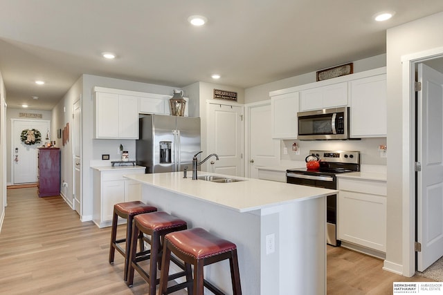 kitchen featuring light countertops, appliances with stainless steel finishes, a kitchen island with sink, a sink, and white cabinetry