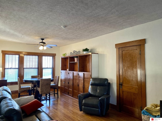 living room with a textured ceiling, wood finished floors, a ceiling fan, and baseboards