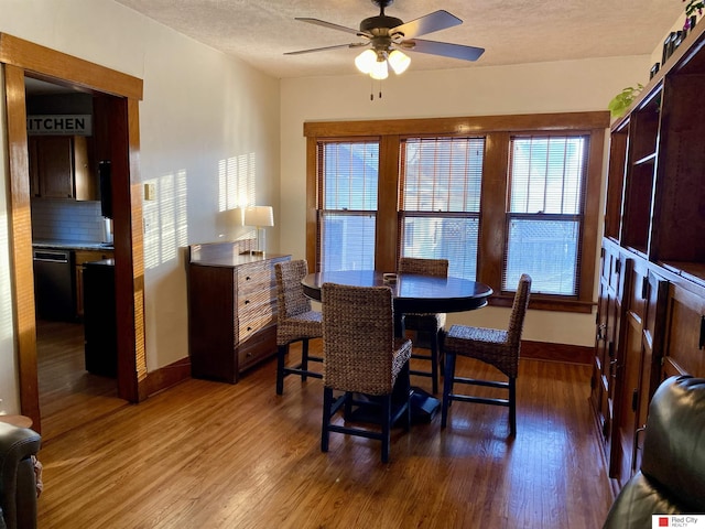 dining space with ceiling fan, a textured ceiling, baseboards, and wood finished floors