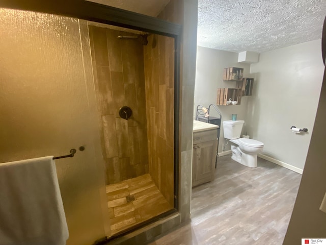 bathroom with a textured ceiling, wood finished floors, vanity, baseboards, and a shower stall