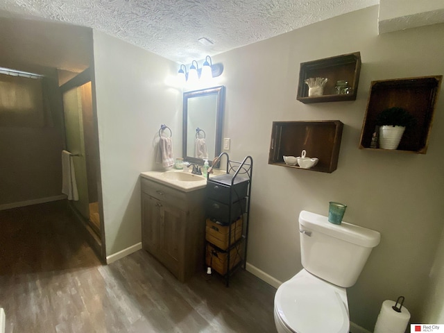 full bathroom featuring toilet, vanity, a textured ceiling, wood finished floors, and baseboards