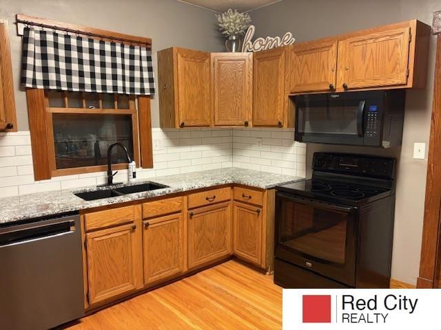 kitchen featuring a sink, light wood-type flooring, light stone countertops, black appliances, and brown cabinetry