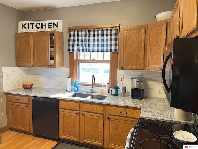 kitchen featuring black appliances, light stone counters, brown cabinetry, and a sink