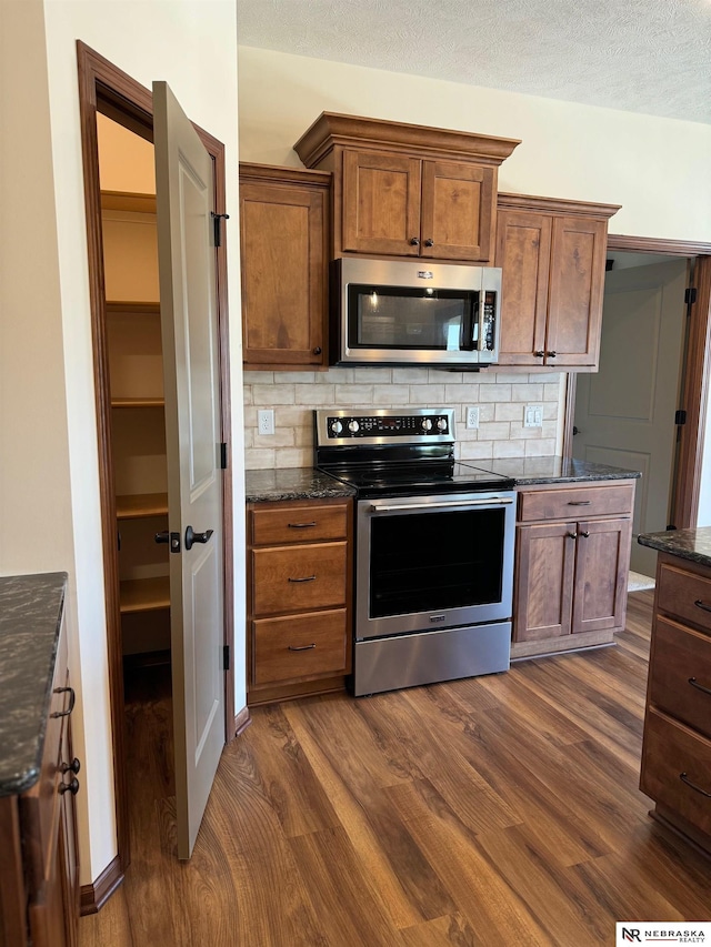 kitchen with dark wood finished floors, decorative backsplash, appliances with stainless steel finishes, a textured ceiling, and dark stone countertops