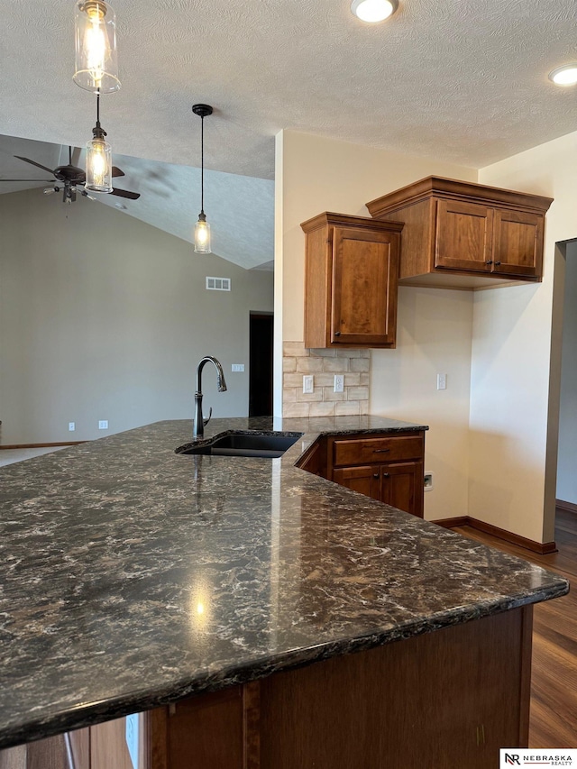 kitchen featuring decorative light fixtures, brown cabinetry, vaulted ceiling, a sink, and a peninsula