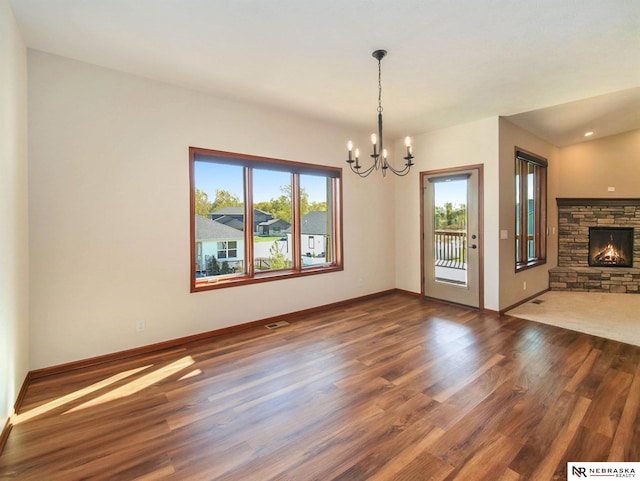 unfurnished living room featuring a notable chandelier, a fireplace, visible vents, baseboards, and dark wood finished floors