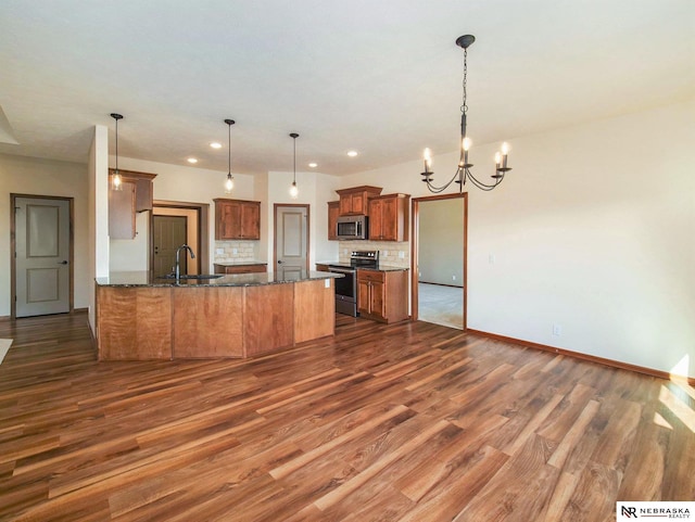 kitchen featuring a sink, appliances with stainless steel finishes, decorative backsplash, brown cabinetry, and decorative light fixtures