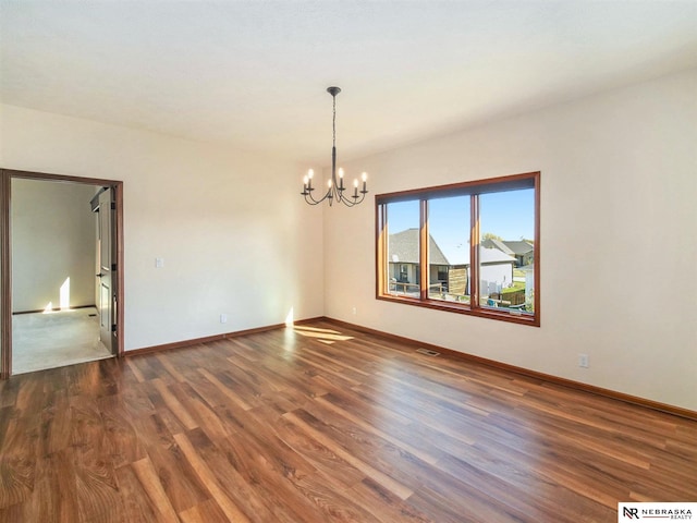 empty room featuring dark wood-style floors, a chandelier, visible vents, and baseboards