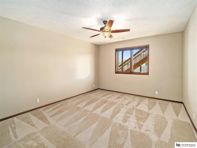 spare room with light carpet, baseboards, and a textured ceiling