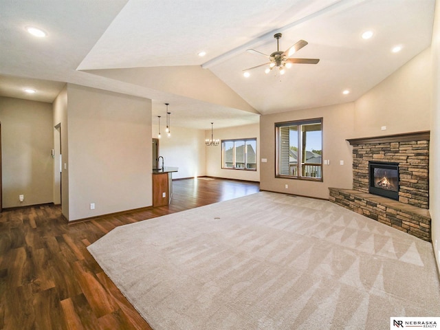 unfurnished living room featuring vaulted ceiling with beams, a stone fireplace, ceiling fan with notable chandelier, and dark wood-style floors