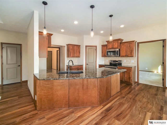 kitchen featuring appliances with stainless steel finishes, brown cabinetry, hanging light fixtures, and a sink