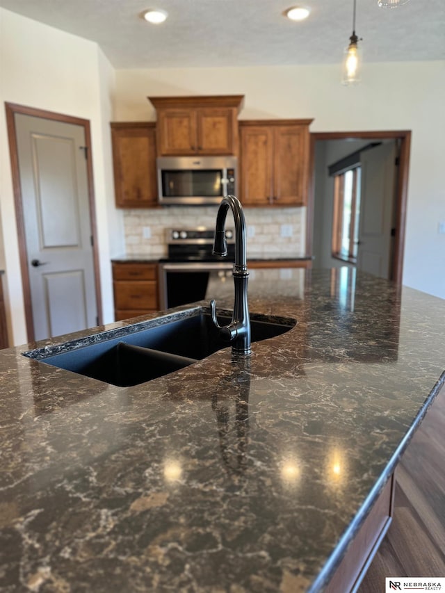 kitchen with hanging light fixtures, stainless steel microwave, dark stone countertops, and brown cabinets