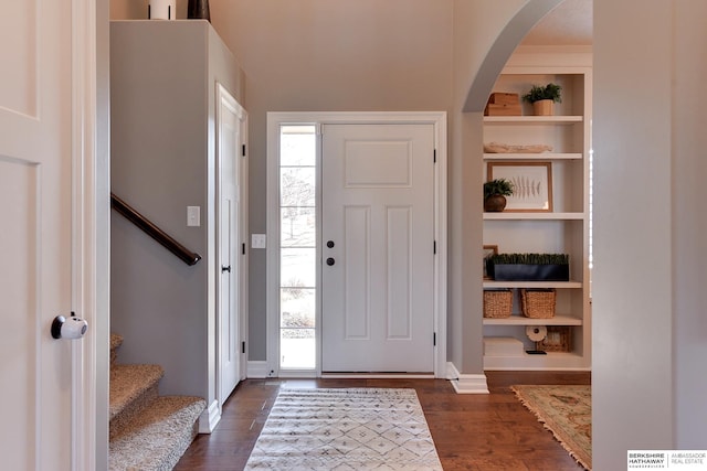 entrance foyer featuring dark wood-type flooring, arched walkways, plenty of natural light, and stairs