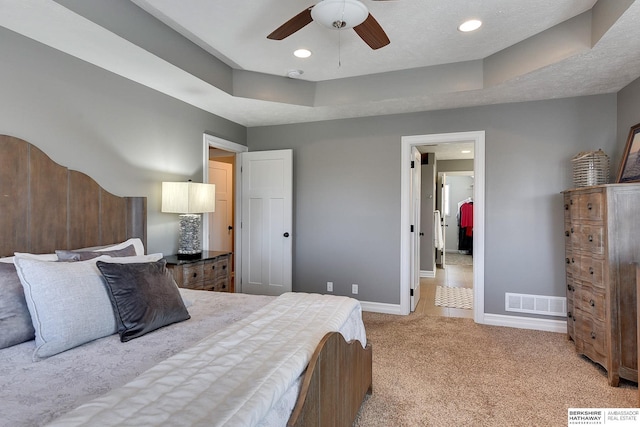 bedroom with a tray ceiling, light carpet, visible vents, and baseboards